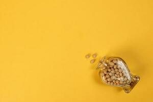 Soyabeans pouring from hart shape glass bottle on yellow background photo