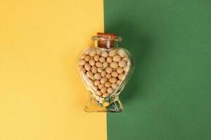 hart shape glass bottle filled with soya beans on yellow background photo