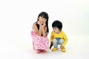 South East Asian young girl boy child brother sister siblings squat siting playing happy posing talking hands on white background photo