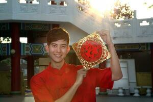 Young south east asian Chinese man traditional costume holding new chinse new year greeting outdoors at temple photo