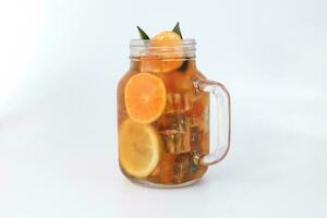 Liquid ice lemon orange tea with slice green leaf cinnamon stick in transparent glass jar mug on white background photo