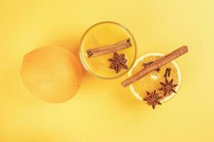 Fresh orange cinnamon star anise clove spice juice in glass on white yellow background photo