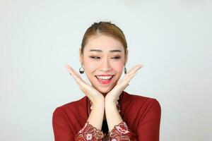 Asian woman traditional red maroon kebaya sharong on white background happy smile surprised hand on cheek photo