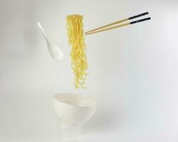 Yellow noodle soup elevated flying suspended in air bowl spoon and chopstick on white background photo