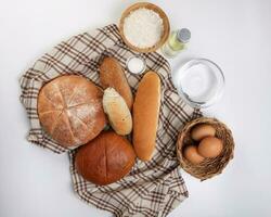 Freshly baked bread loaf bun roll round long mix verity wrapped in checkered kitchen fabric napkin towel wheat flower oil water salt eggs over white background photo