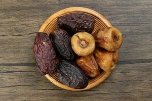 Ripe juicy dates fruit khurma variety black yellow on wooden saucer over rustic wood background photo