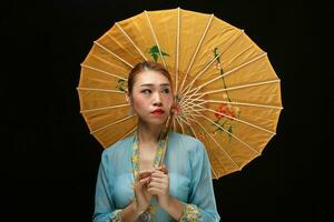 Asian woman in tractional kebaya behind umbrella on black background photo