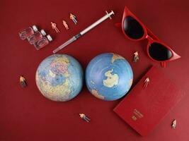 Vaccine passport red sunglass world atlas globe map north south pole on red paper background world travel tour vacation mini human figures medical needle syringe bottle photo