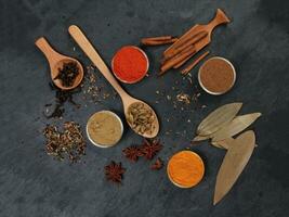 Mix variety spice cinnamon cardamom clove bay leaf wooden chilli cumin turmeric powered on black slate background photo