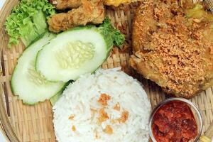 Ayam penyet a East Javanese cuisine smashed fried chicken dish with floss sambal slices of cucumbers fried tofu and tempeh photo