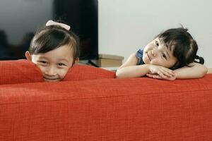 Two little girl child happy smile looking over the sofa photo