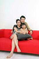 South East Asian young couple father mother daughter parent girl child on red sofa look at camera on white background photo