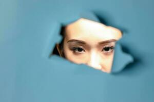 Young beautiful Asian woman expression through torn paper hole photo