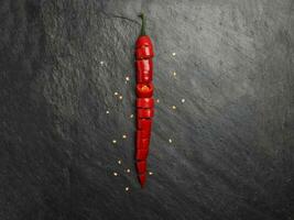 Red hot chilli pepper on dark black rough slate stone surface background photo