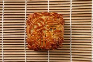 Chinese baked decorated mooncake mid autumn festival square moon cake filling gift wish offering on bamboo mat over wooden table mini cup photo