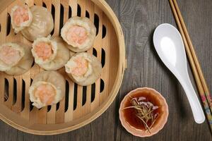Prawn shrimp shaomai dim sum dumpling in bamboo steamer sauce chopsticks soup soon on rustic wood background photo