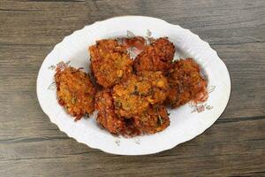 Deep fried piaju onion fitter bhajia on decorated ceramic plate over rustic wooden background photo