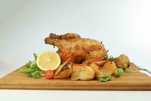 Whole roasted grilled chicken poultry bird with baked potato vegetable salad tomato lemon on wooden cutting board white background photo