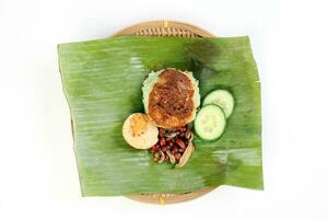 Nasi Lemak fragrant rice cooked in coconut milk served with sambal friend peanut anchovy boiled egg packed in banana leaf on round bamboo plate on white background photo