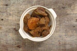 Asian style Beef bhuna dry curry with potato in ceramic bowl over rustic wooden background photo
