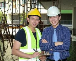 sur este asiático joven malayo chino hombre vistiendo blanco amarillo la seguridad casco chaleco Corbata estudiar ver hablar portapapeles al aire libre construcción sitio Mira a cámara foto