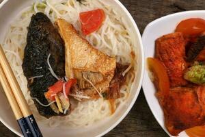 Fish head noodles vermicelli milk soup in white bowl pan friend salmon fish fillet on triangular plate chopstick spoon on rustic wooden background photo