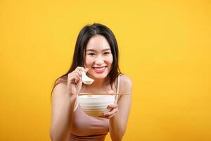 Beautiful young south east Asian woman holding chines empty chopstick Chinese soup spoon bowl utensil pretend acting posing see eat taste smell feed offer satisfaction yummy yellow orange background photo