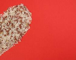 Mixed low glycaemic index healthy rice grain basmati millet buckwheat red rice half hart shape on red background photo