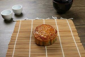 Chinese baked decorated mooncake mid autumn festival round moon cake filling gift wish offering on bamboo mat over wooden table mini cup photo
