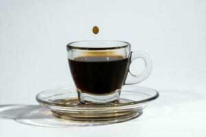 Coffee droplet on transparent glass espresso cup saucer full of liquid coffee on white background photo