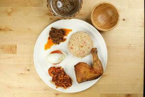 Indonesian royal dish nasi bojari with deep spiced deep fried chicken leg sambal prawn curry beef rendang boild egg cucumber and tomato slice photo