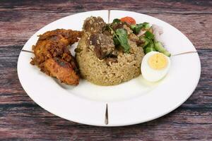 Beef Biryani Tehari with boiled egg coriander leaf garnish chicken curry pot roasted leg tomato cucumber onion chili coriander salad on white plate set over rustic wood background photo