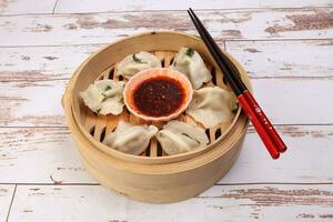 Home style dim sum dumpling in bamboo steamer chopsticks chili flake oil sauce on rustic wooden background photo