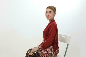 Asian woman traditional red maroon kebaya sharong on white background sitting pose chair sit photo