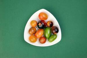 Red orange yellow green tomato mix variety on white triangle shape plate over green paper background photo