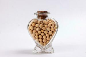Soya beans in a hart shape glass bottle on white background photo