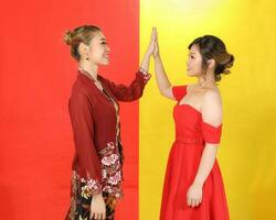 Two Asian woman traditional kebaya and modern dress red yellow paper background hands high five photo