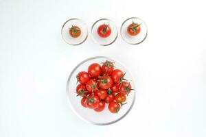 Red ripe cherry tomato with stem in mini glass bowl on white background photo