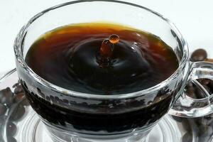 Coffee splash pillar in transparent glass cup saucer full of liquid coffee on white background photo