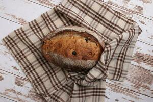 Rustic whole grain artisan bread loaf with cranberry raisin dry fruit nuts wrapped in checkers cloth with wooden table top flat lay view photo