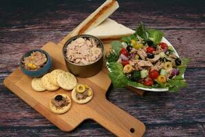 Tin can tuna fish meat chunk flake product recipes salad spread topping tapas cracker sandwich on wooden black slate board over rustic wooden table photo