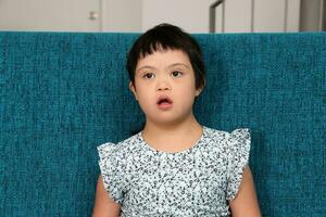 Southeast Asian small little girl child sitting on blue sofa look happy smile pose. She have down syndrome photo