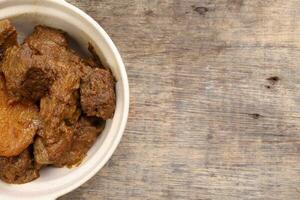 Asian style Beef bhuna dry curry with potato in ceramic bowl over rustic wooden background photo