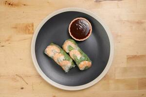 Vietnamese prawn shrimp see through rice paper spring roll green vegetable sauce on dark plate on wooden table photo