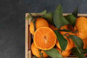 mandarin orange green leaf in wooden box crate top view on black slate marble background photo