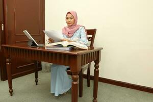 joven asiático malayo musulmán mujer vistiendo Pañuelo a hogar oficina estudiante sentar a mesa computadora libro archivo papel estudiar trabajo foto