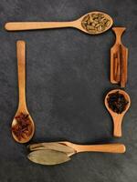 Mix variety spice cinnamon cardamom clove bay leaf wooden spoon border frame copy text space on black slate background photo