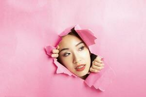 Young beautiful Asian woman expression through torn paper hole photo