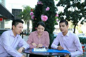 Young south east Asian middle eastern man woman business colleague outdoor cafe chair table meeting talking discussing file paper photo