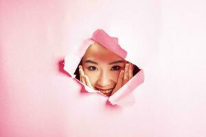 Young beautiful Asian woman expression through torn paper hole photo